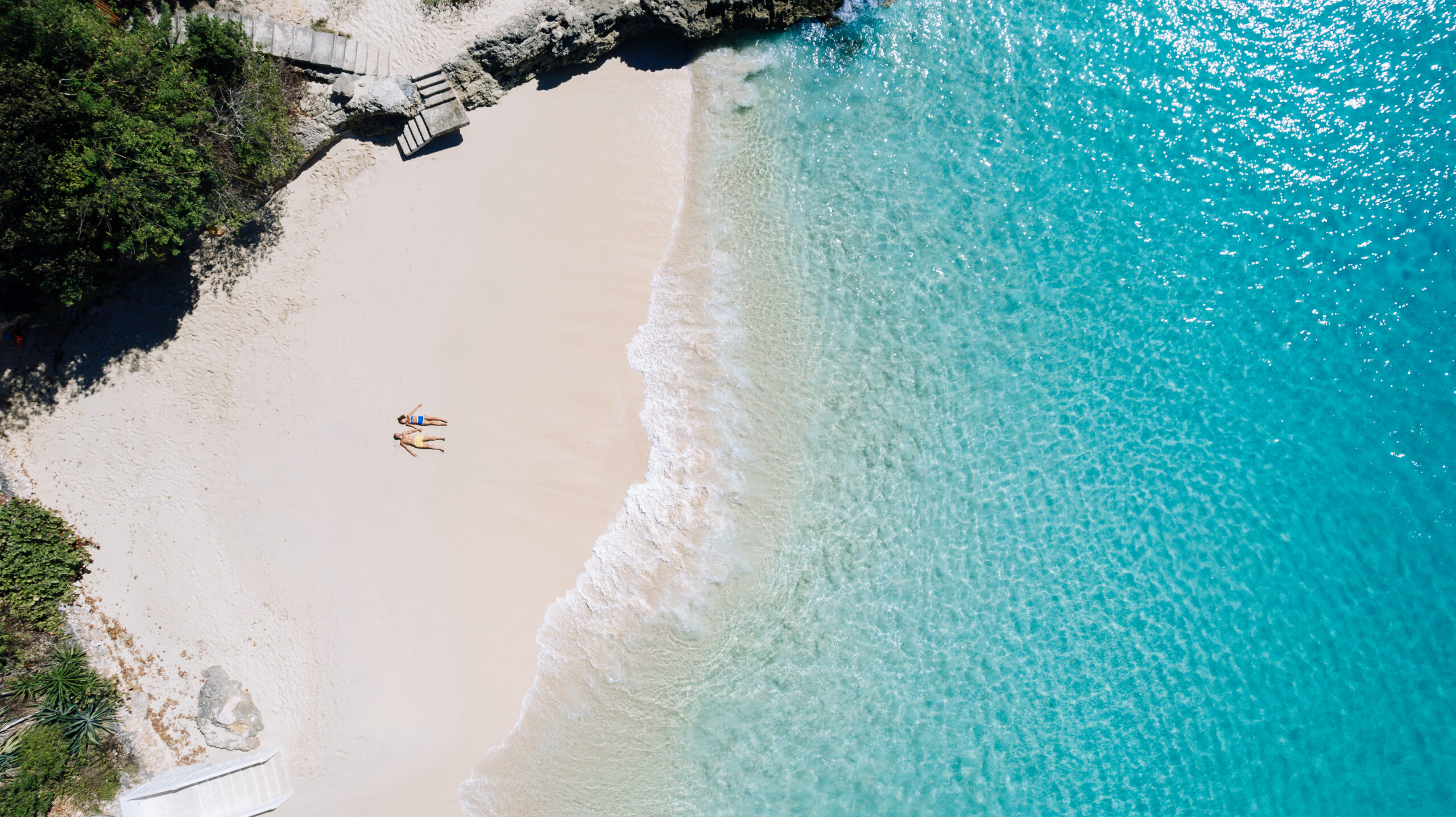 Aerial view of two sunbathers on the pristine beach at Malliouhana, Anguilla, with turquoise water.
