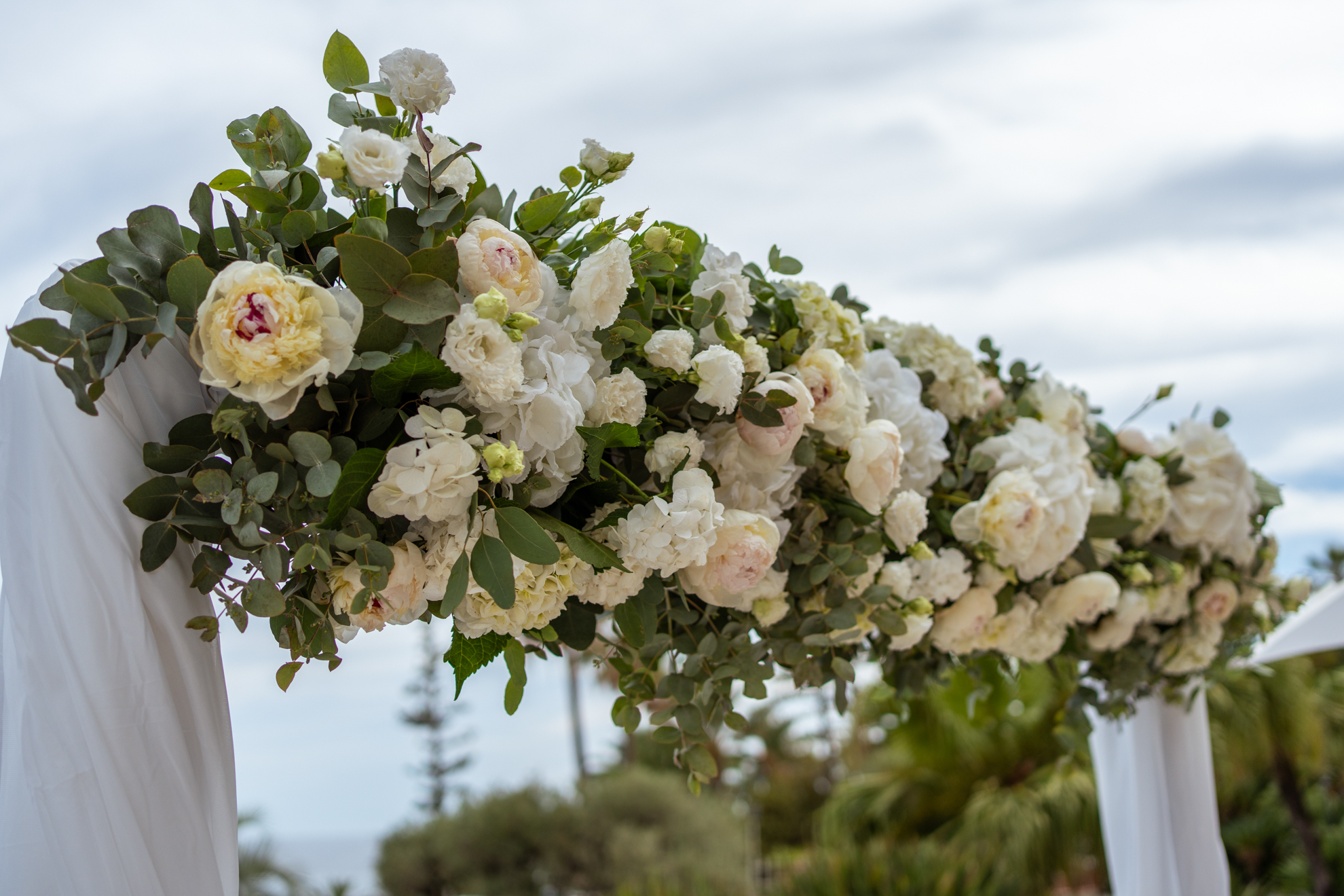 Elegant floral arrangement on a wedding arch, featuring white flowers and greenery.