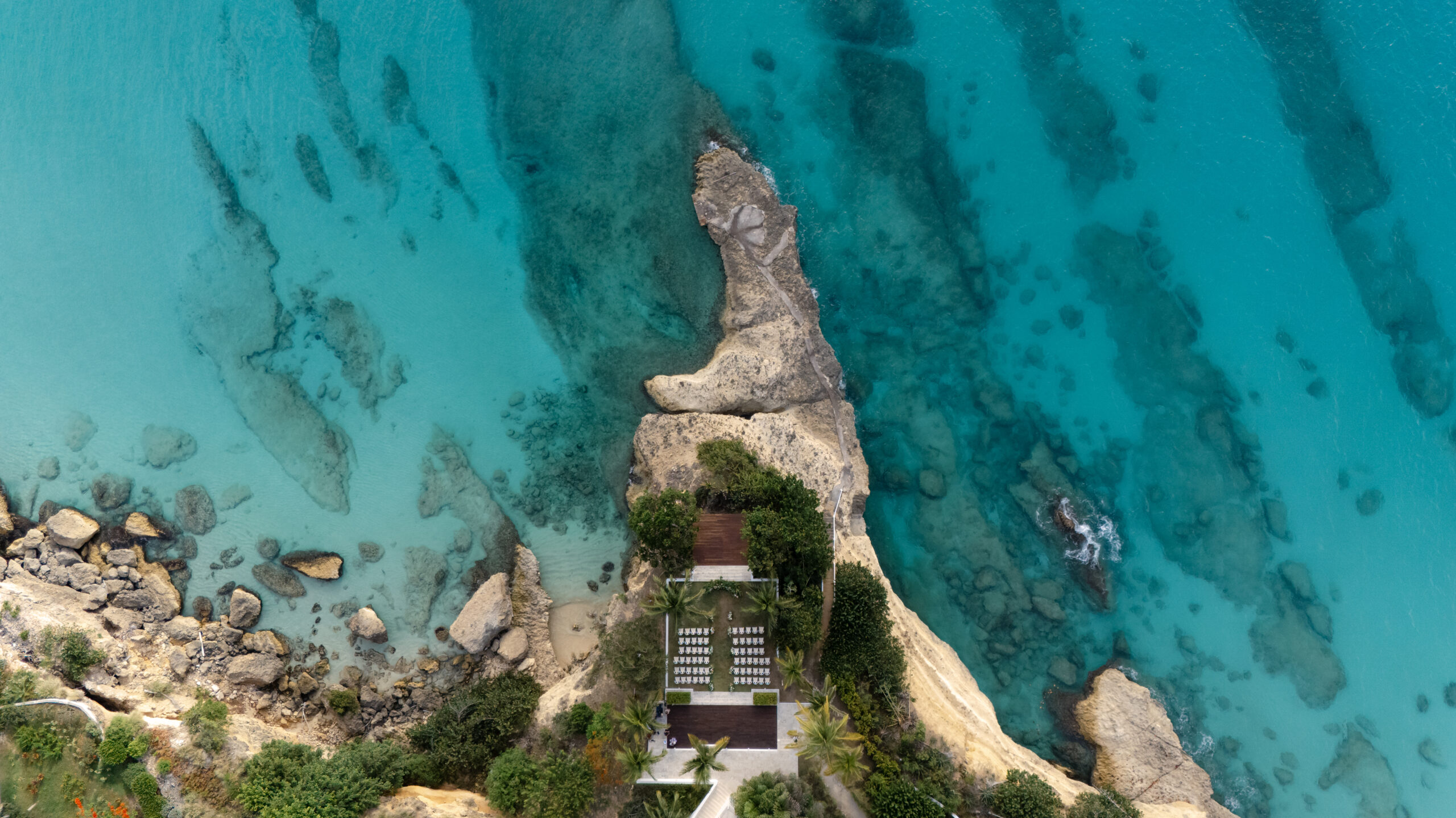 Aerial view of Malliouhana resort wedding setup on a rocky point, turquoise ocean surrounding.
