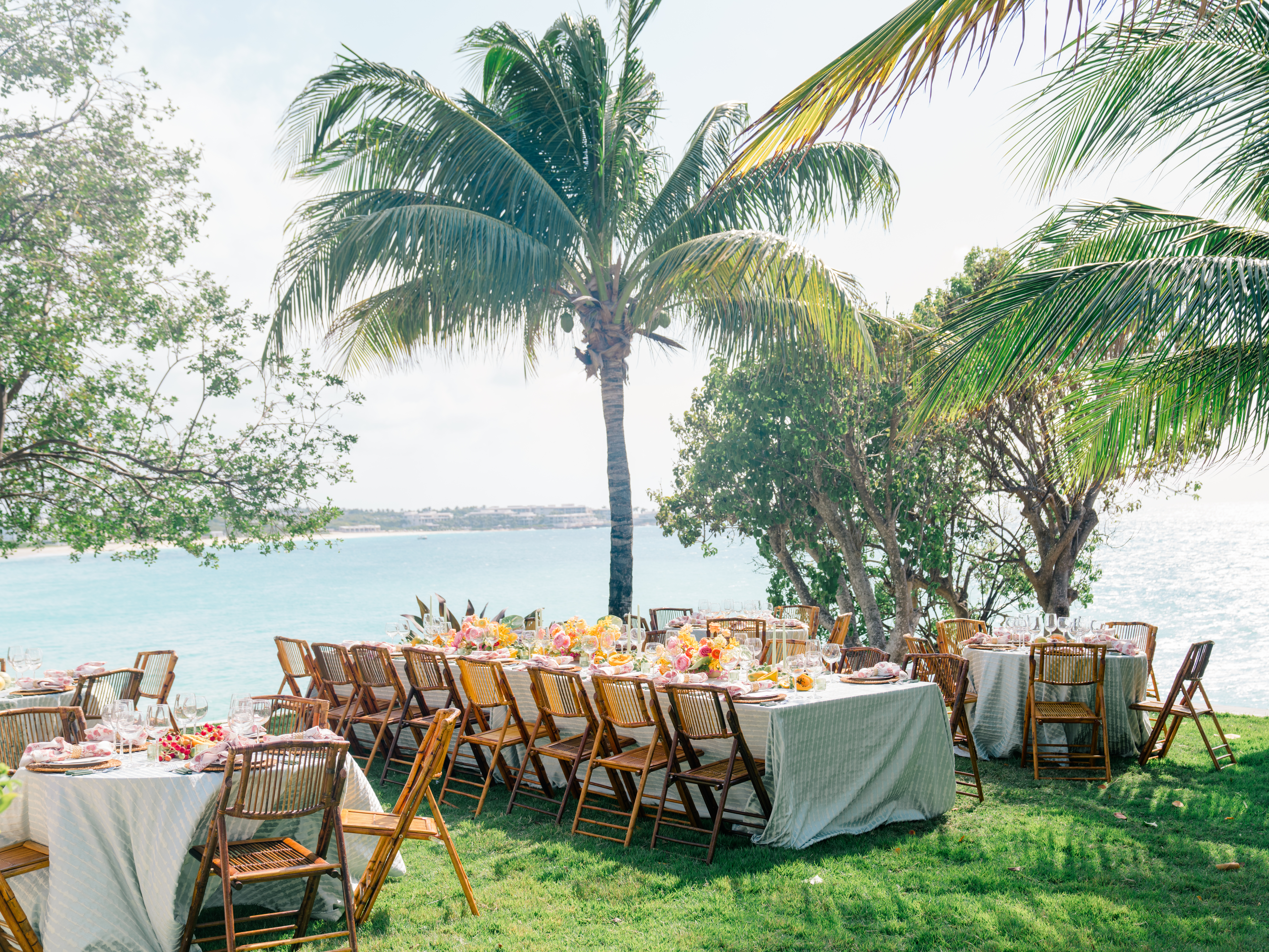 Outdoor dining setup with tables under palm trees overlooking the ocean