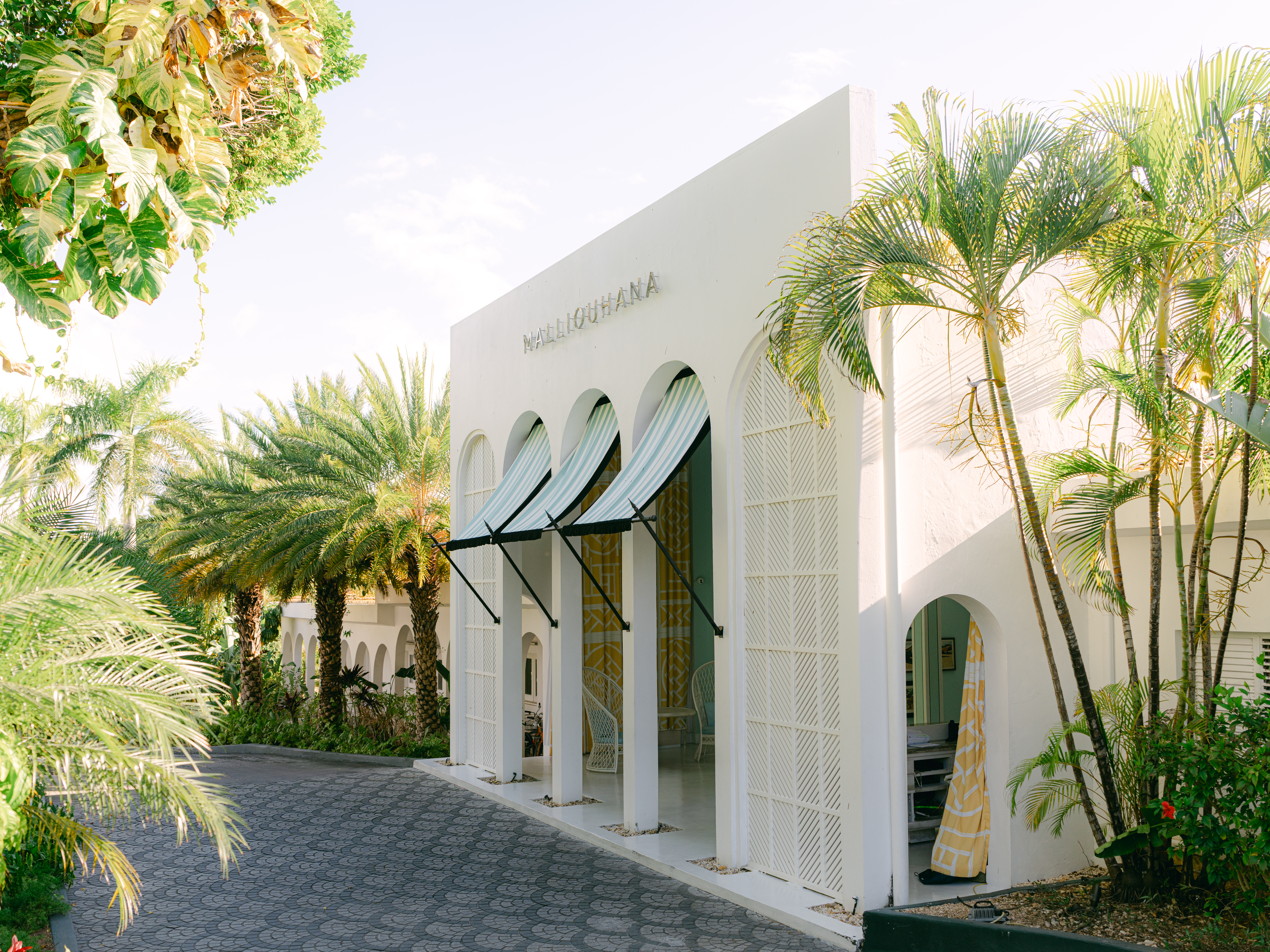 Tropical hotel entrance with arched windows and palm trees at Malliouhana