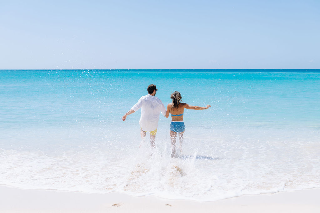 Couple running into turquoise ocean at Malliouhana beach. White sand and blue sky.