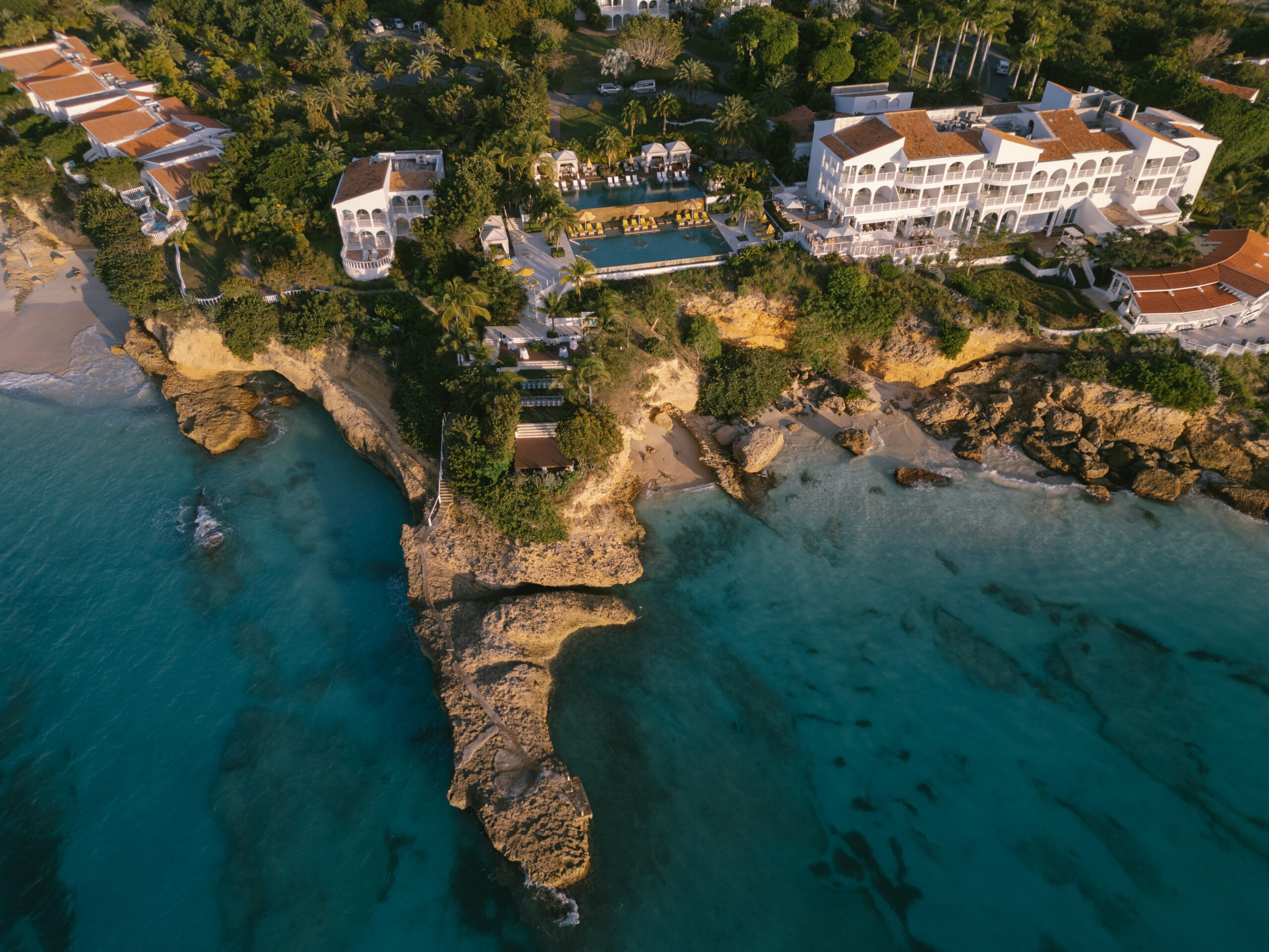 Malliouhana resort on a cliff overlooking turquoise water and a sandy beach.