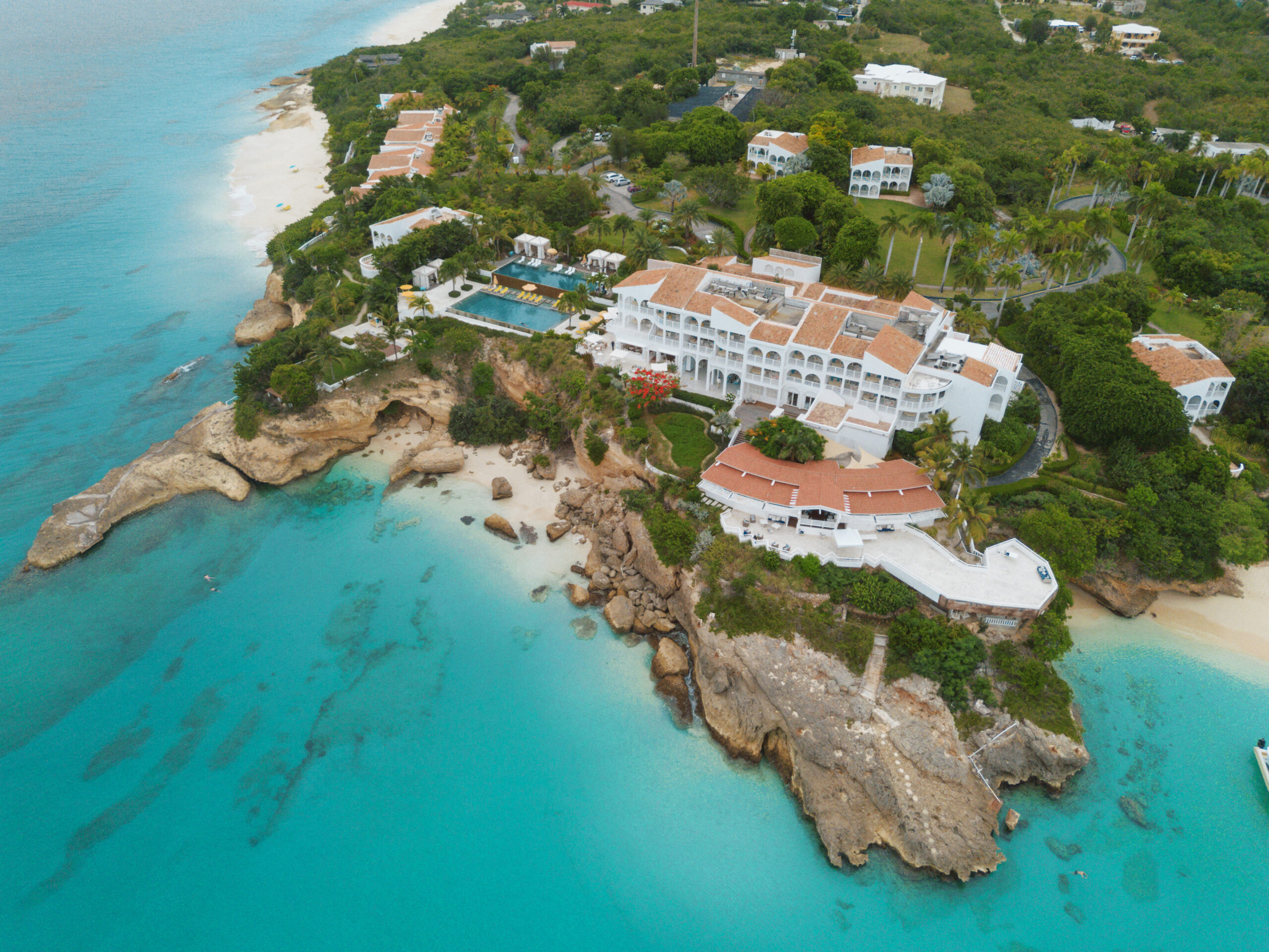 Malliouhana resort on a cliff overlooking turquoise water and a sandy beach.