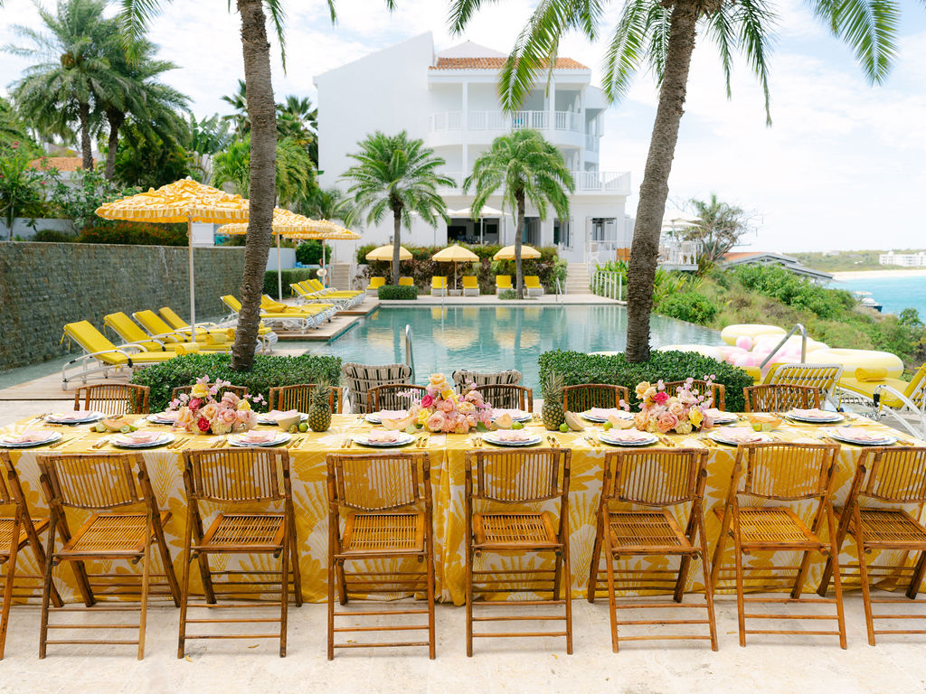 Outdoor dining table at Malliouhana resort by the pool, with yellow umbrellas and palm trees.
