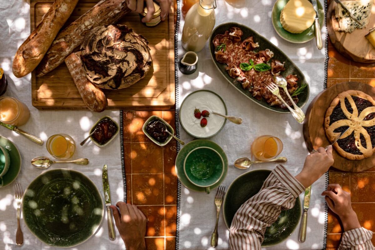 Overhead shot of a lavish brunch spread with bread, charcuterie, and dessert. Luxury villa rentals provide settings for such feasts.