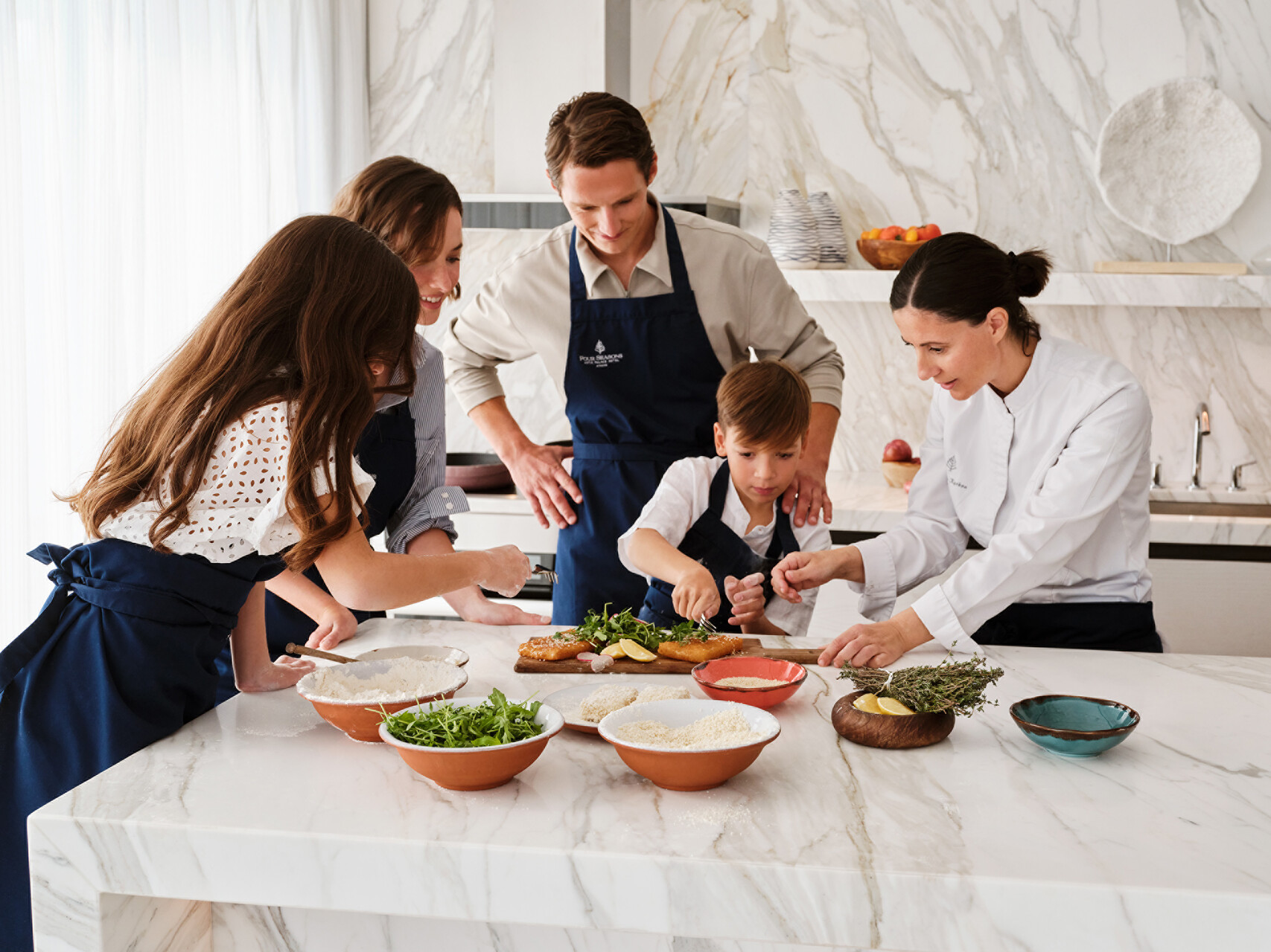 Family cooking class at Four Seasons Astir Palace Hotel Athens. Chef assisting boy with food prep.