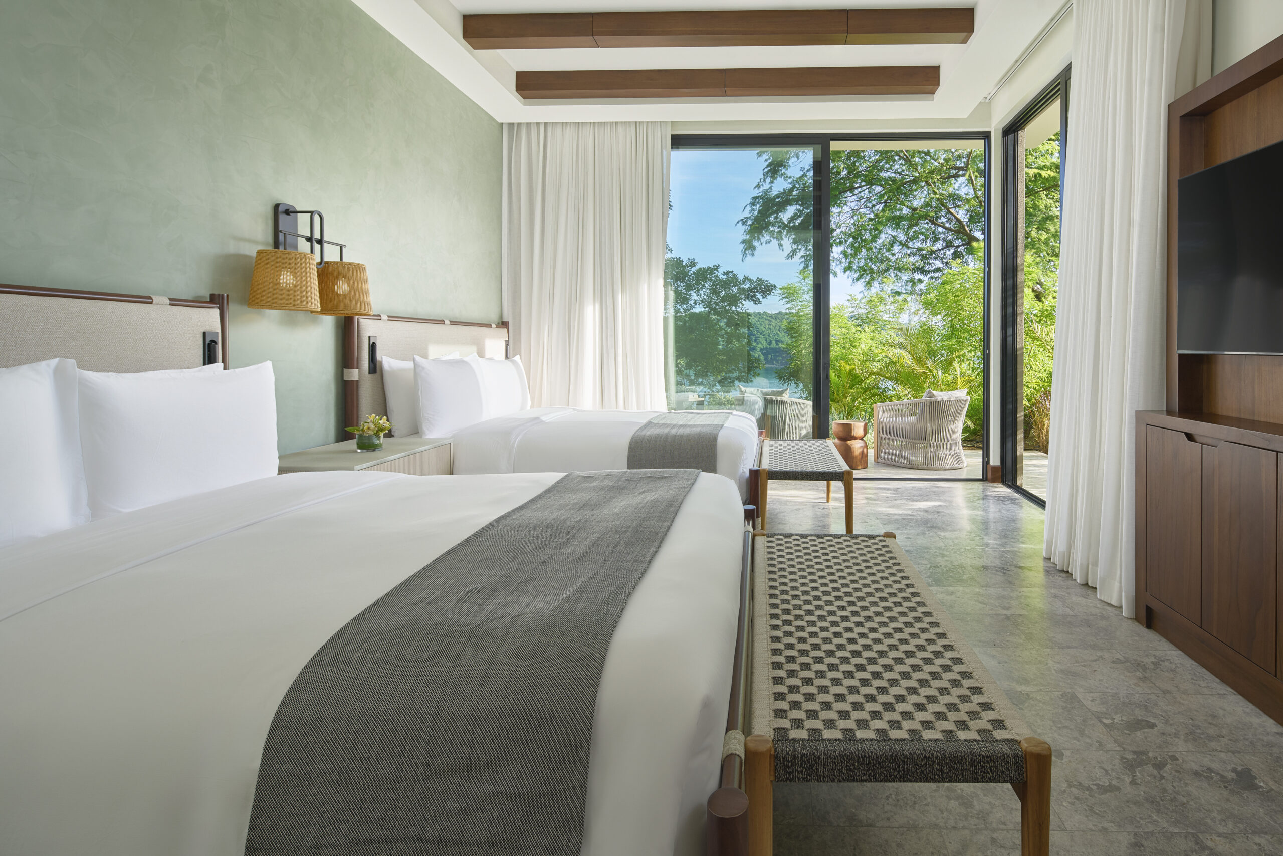 Two beds in a bright room at Nekajui, a Ritz Carlton Reserve, with patio view.
