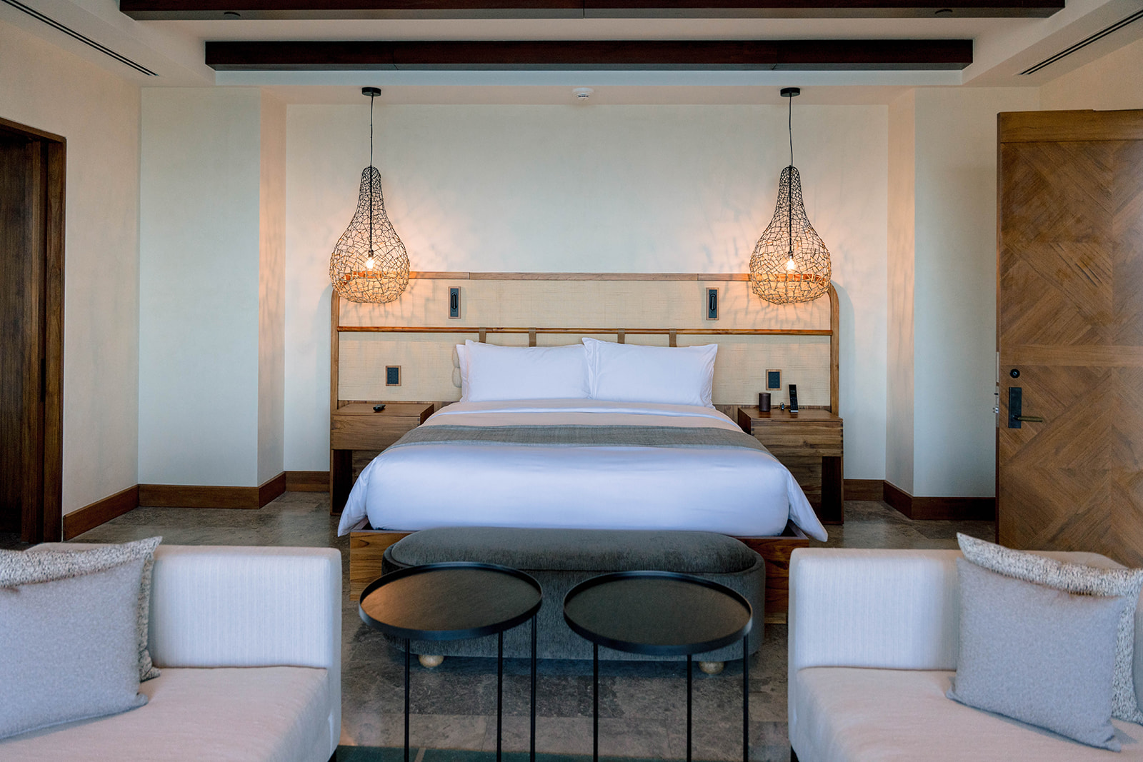 Nekajui Ritz Carlton Reserve suite with a king bed, woven headboard, and hanging pendant lights.