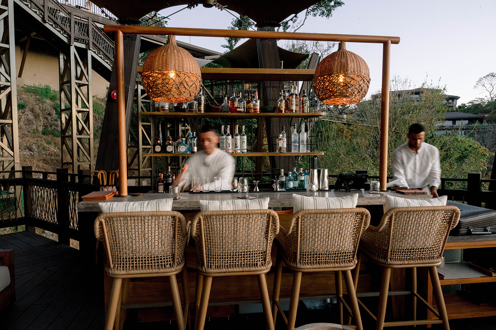 Open-air bar at Nekajui, a Ritz Carlton Reserve, with two bartenders and woven bar stools.