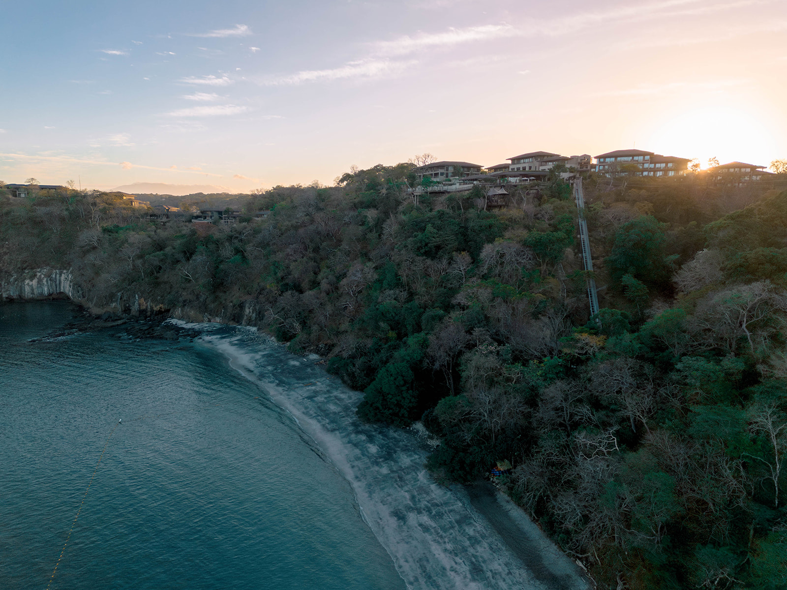 Nekajui Ritz Carlton Reserve aerial view of beach and hillside villas at sunset.