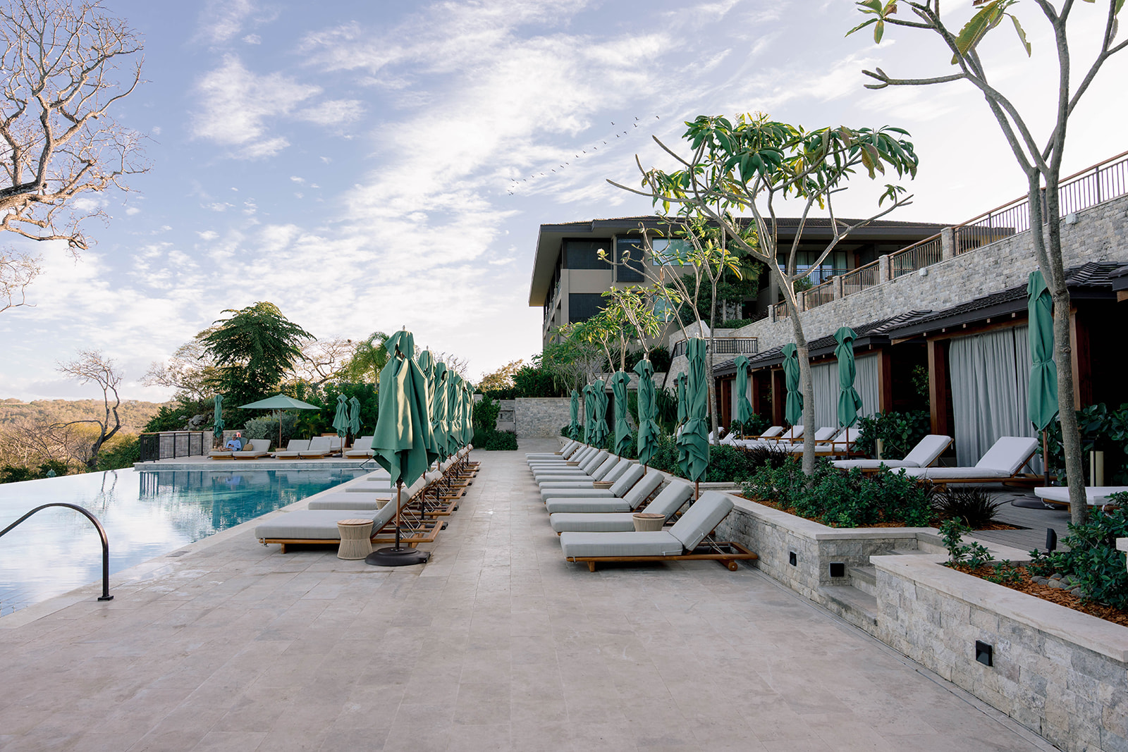 Nekajui, a Ritz Carlton Reserve pool with lounge chairs and umbrellas under a partly cloudy sky.
