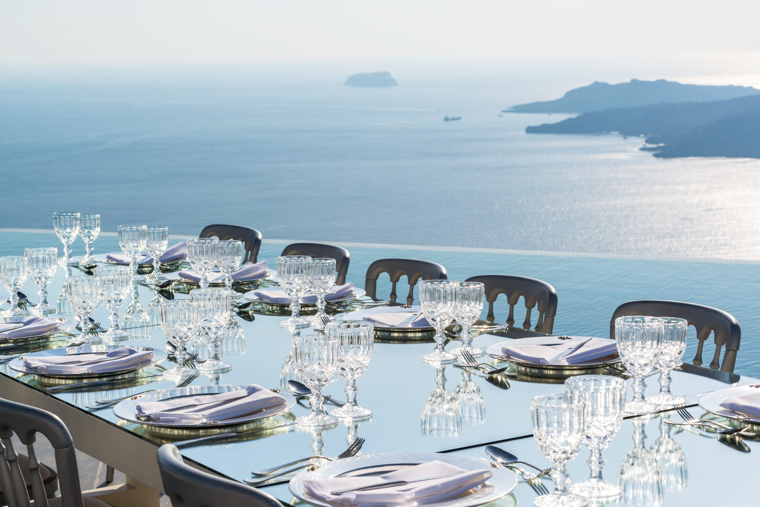 Elegant dining table set for a celebration on a balcony overlooking the sea in Santorini.