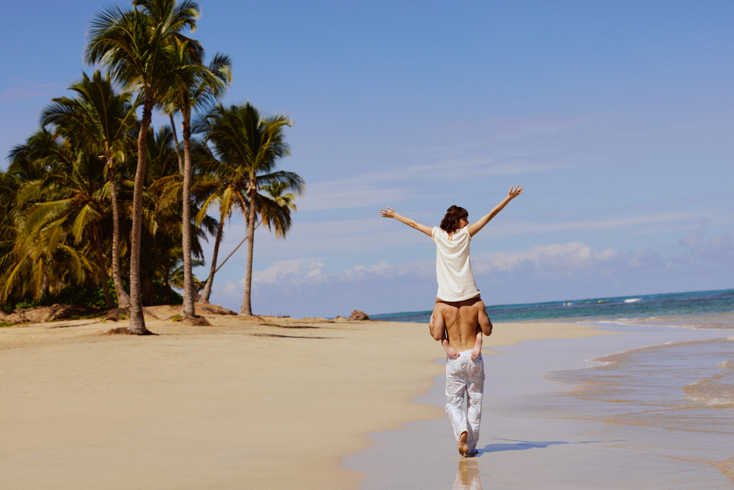 Couple enjoying the beach at W Punta Cana, with woman on man's shoulders under palm trees.