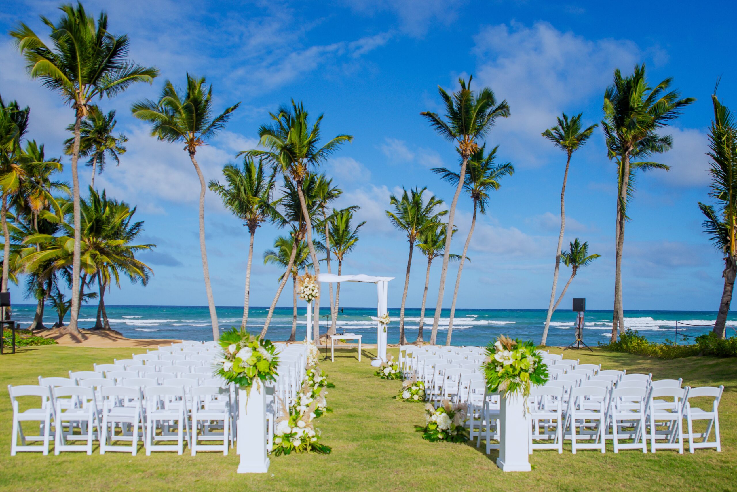 Beach wedding at W Punta Cana with white chairs, altar, and palm trees against a blue sky.