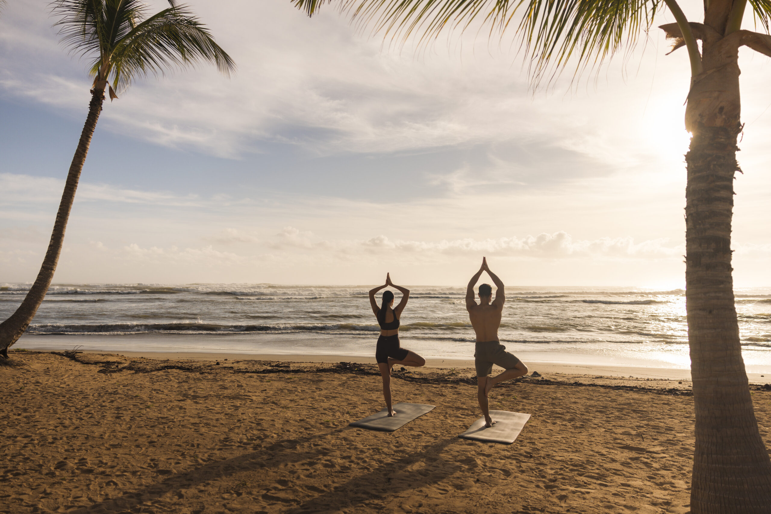Couple doing yoga on the beach at W Punta Cana, with palm trees and ocean view.