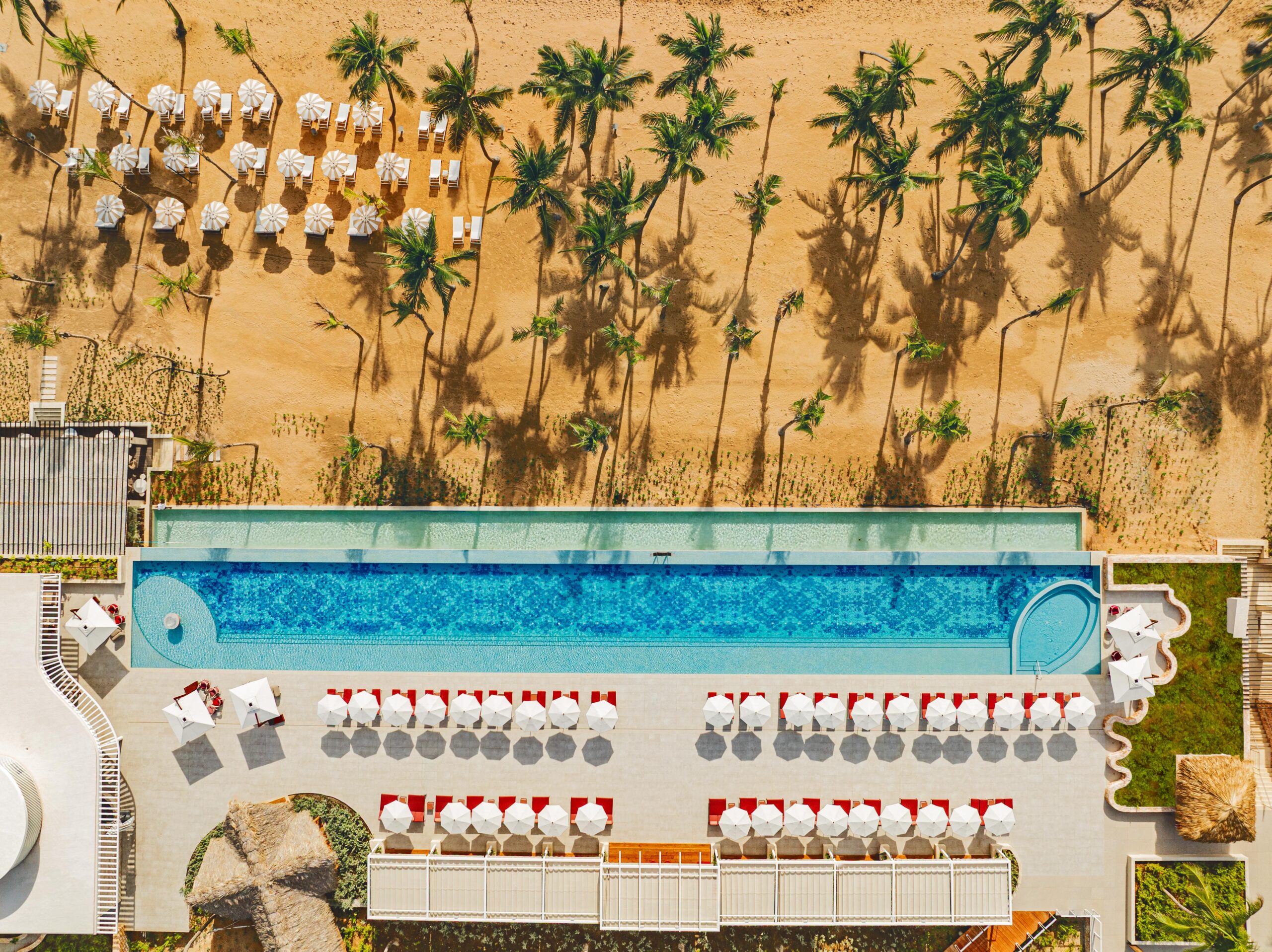 Aerial view of the W Punta Cana resort, featuring a long pool, beach umbrellas, and palm trees.