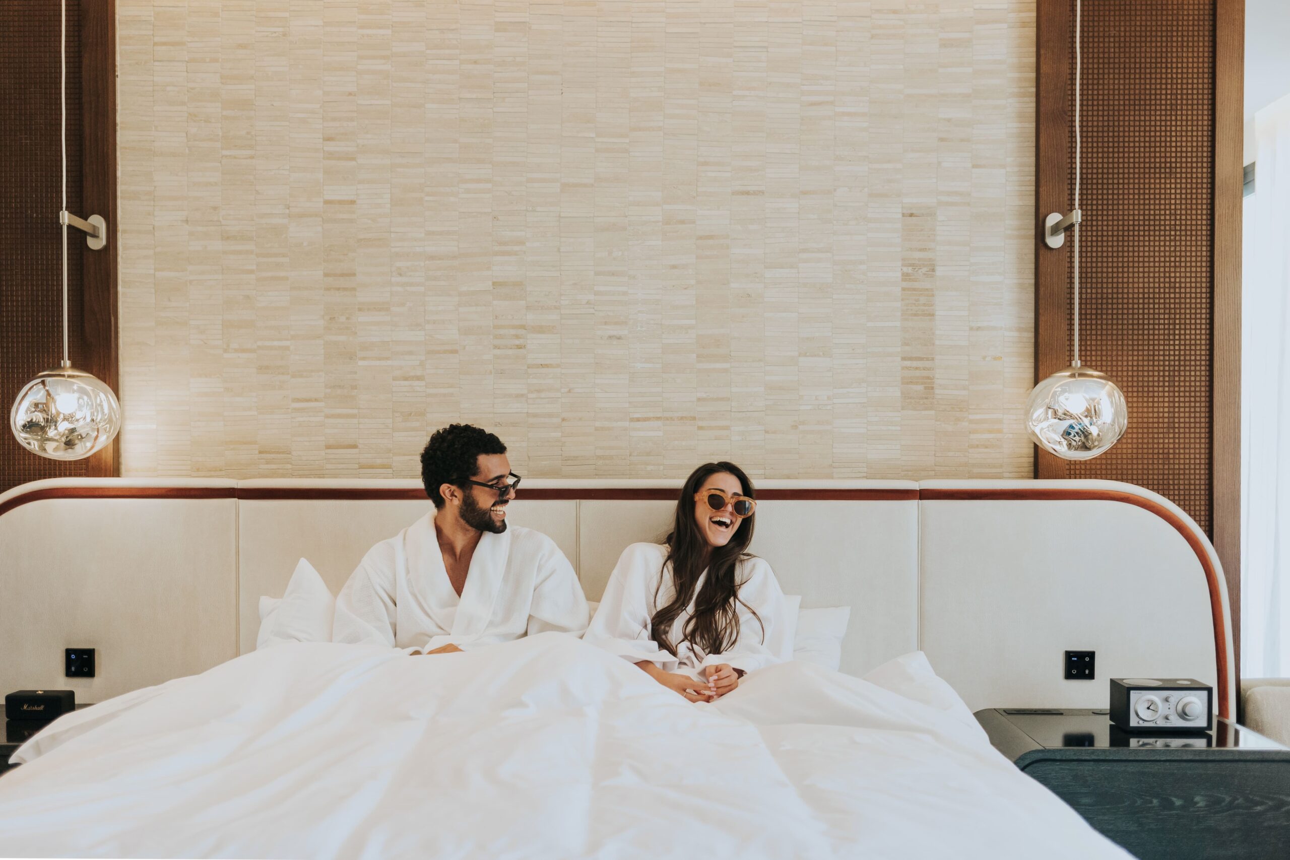 Couple in bathrobes laughing in bed at W Punta Cana, adult all-inclusive resort.