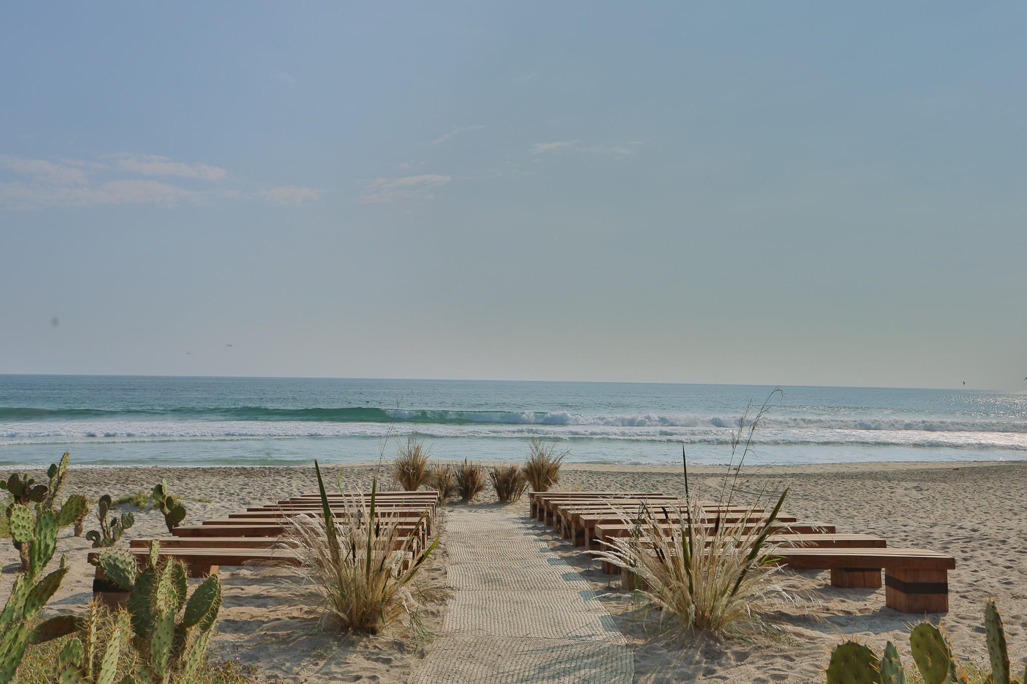 Beach wedding setup with wooden benches and aisle at Hotel Casa Yuma