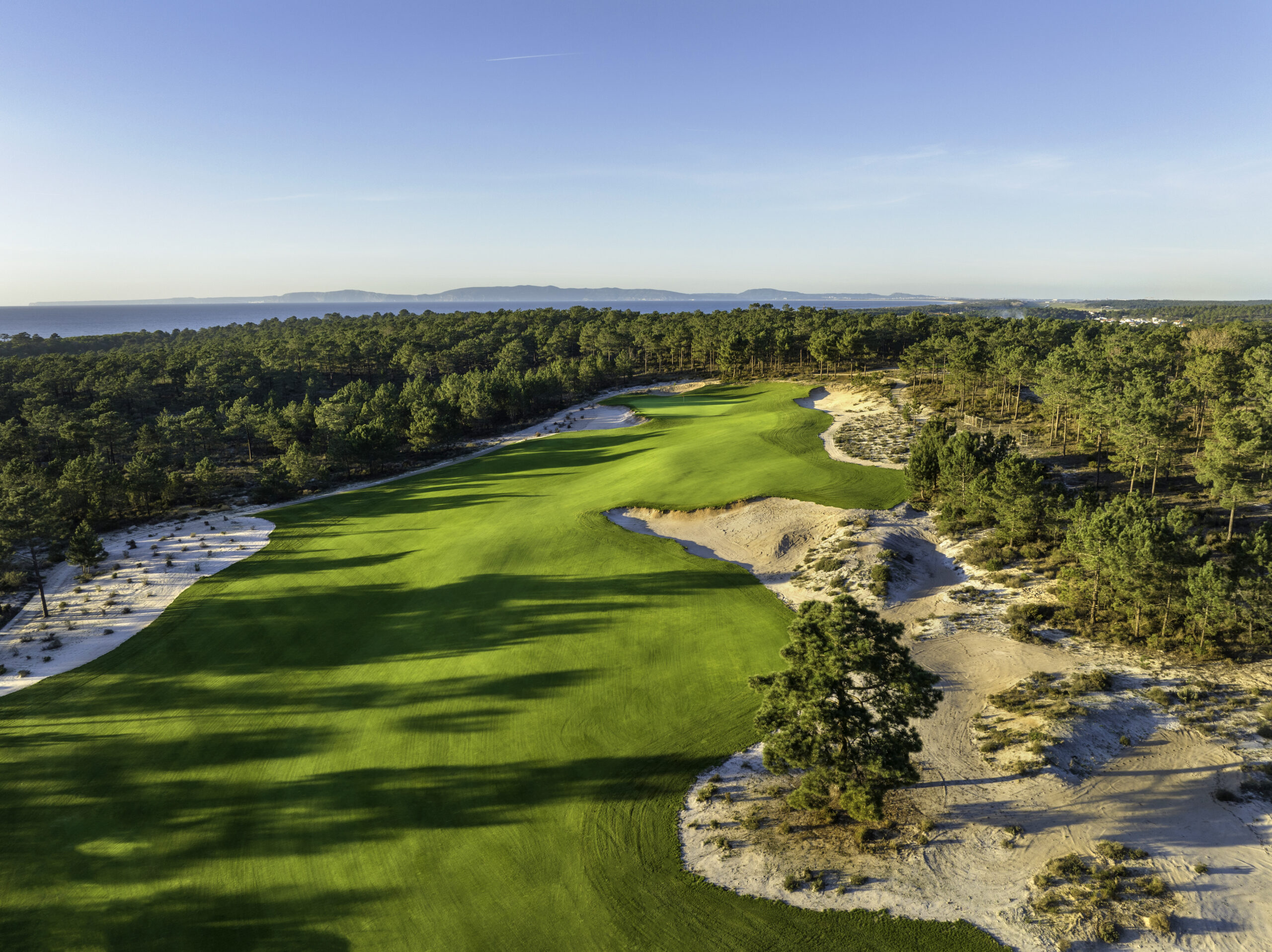 Aerial view of a lush green golf course in Comporta, Portugal, with pine trees and sand dunes