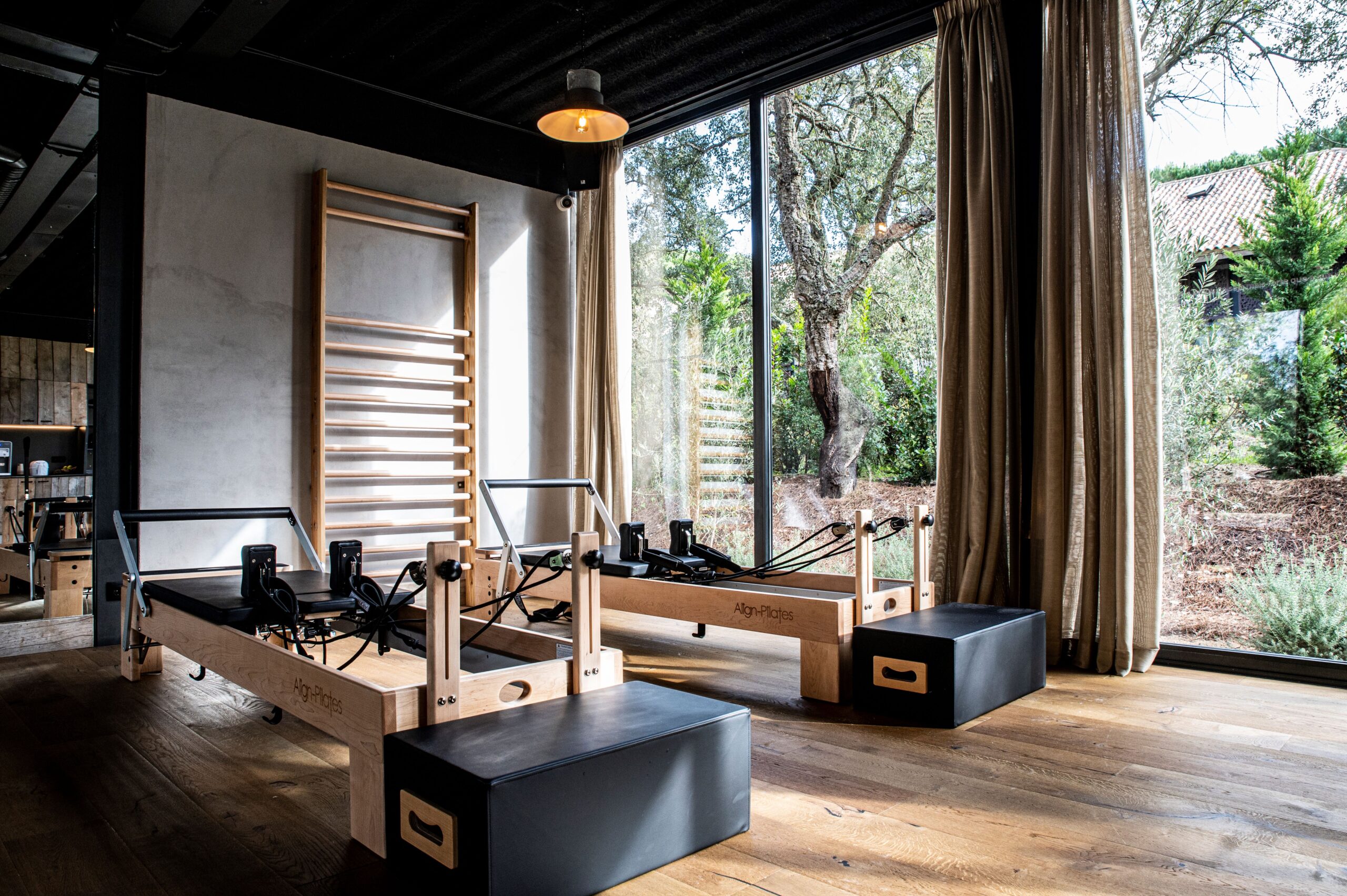 Pilates studio with reformers and wall ladder, natural light, large windows with garden view.