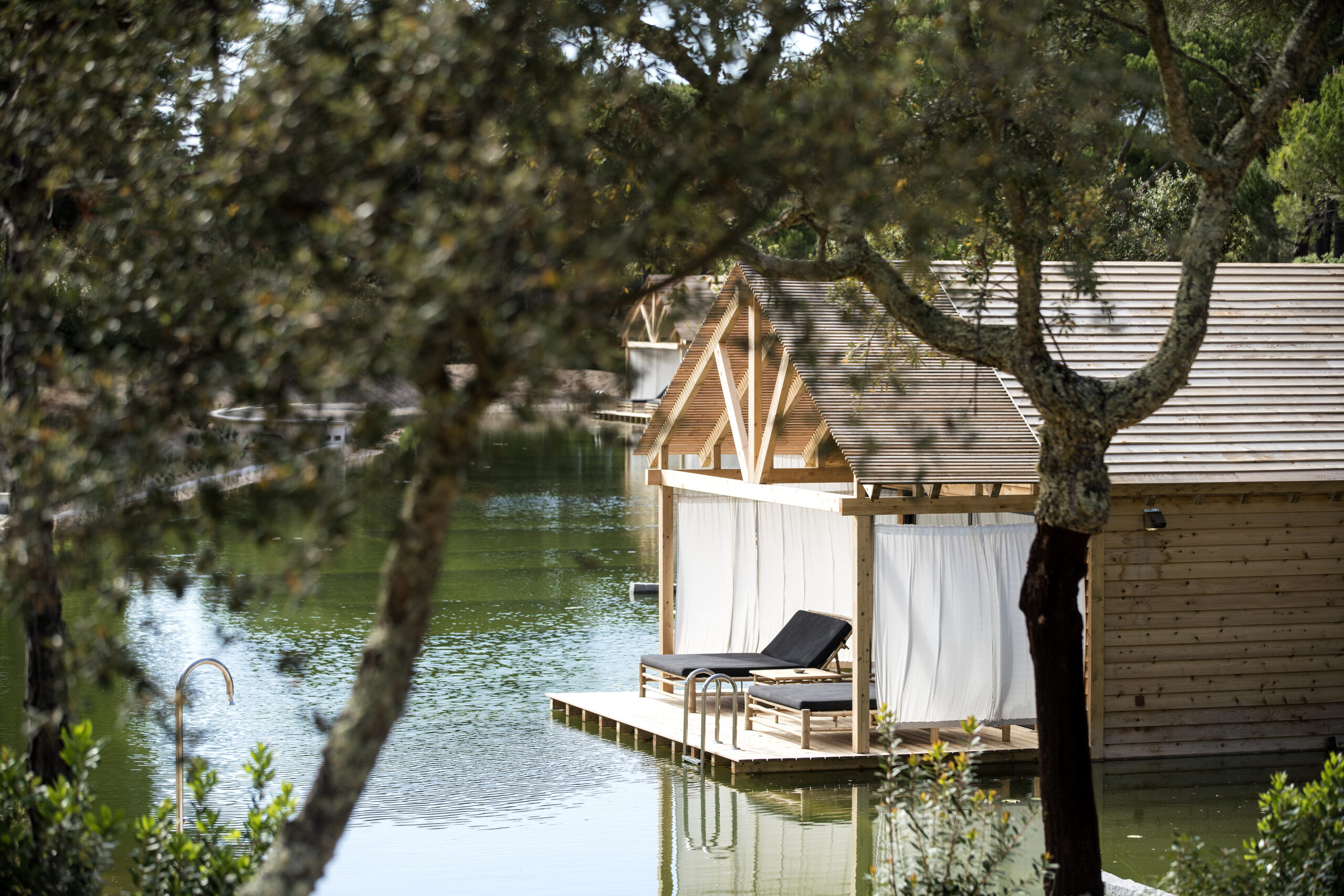 Wooden cabins with lounge chairs on a deck by a tranquil lake at Sublime Comporta