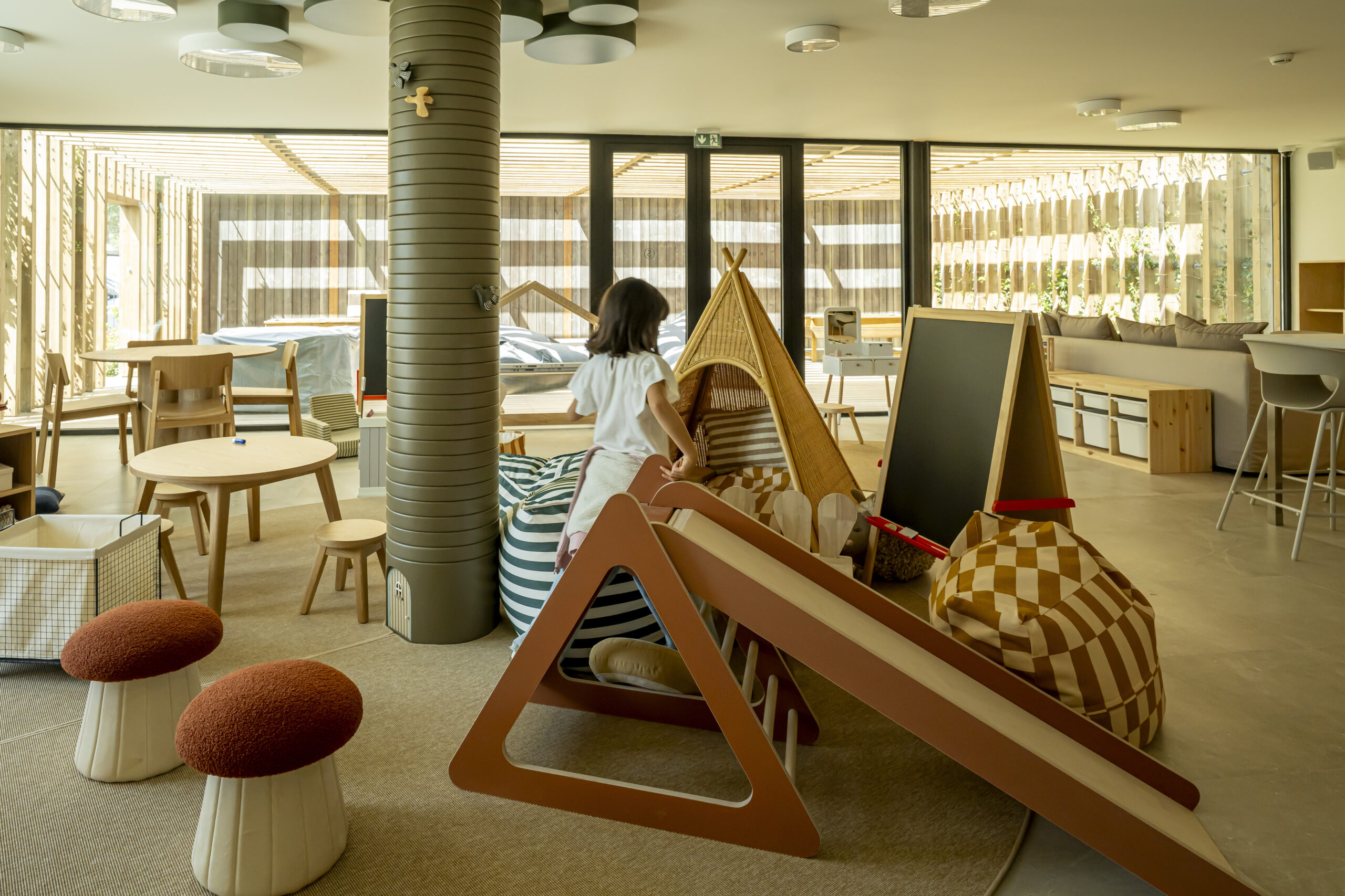 Child playing in a brightly lit modern kids' play area with teepee and slide.