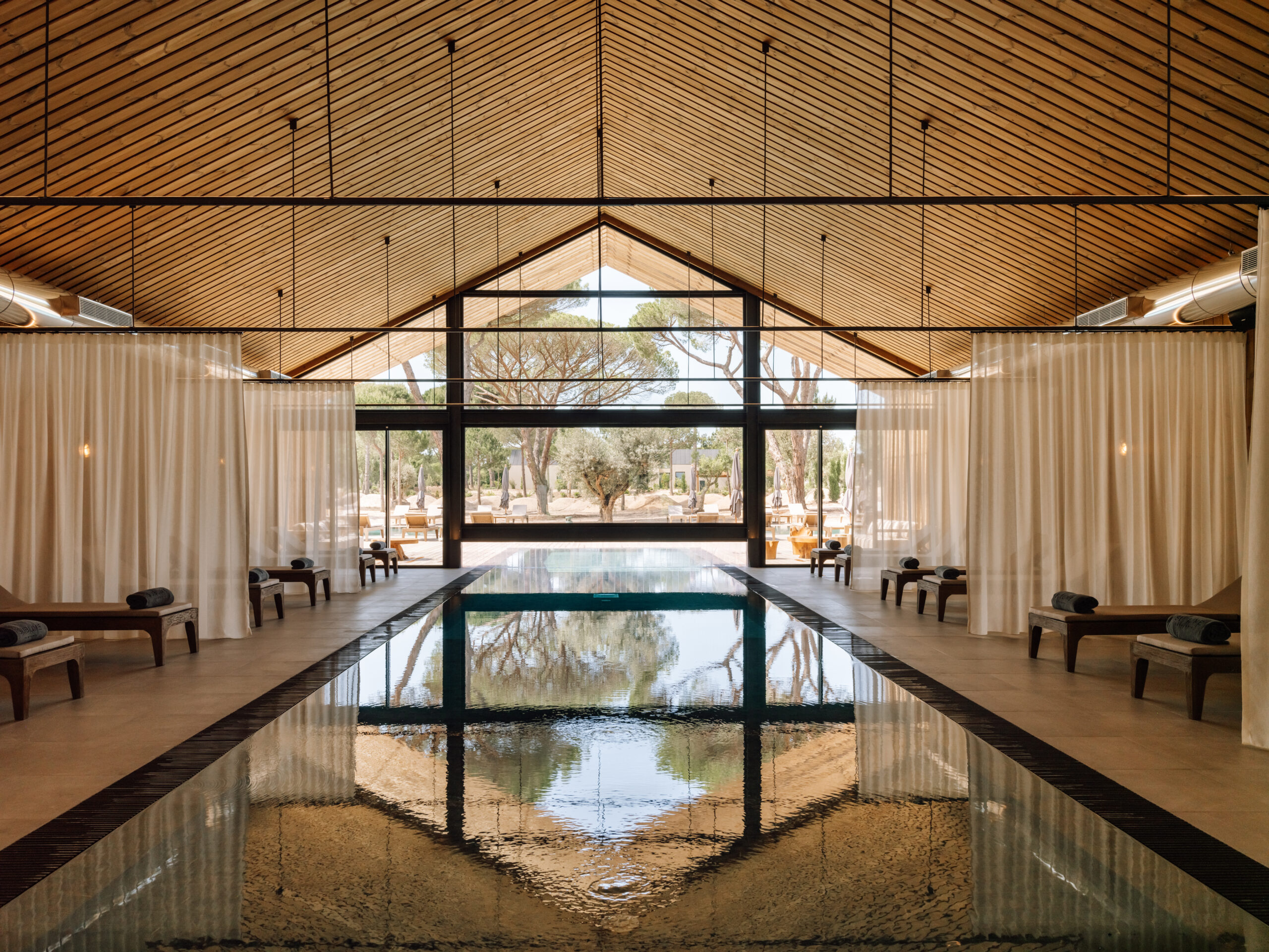 Indoor swimming pool with lounge chairs and large windows overlooking trees