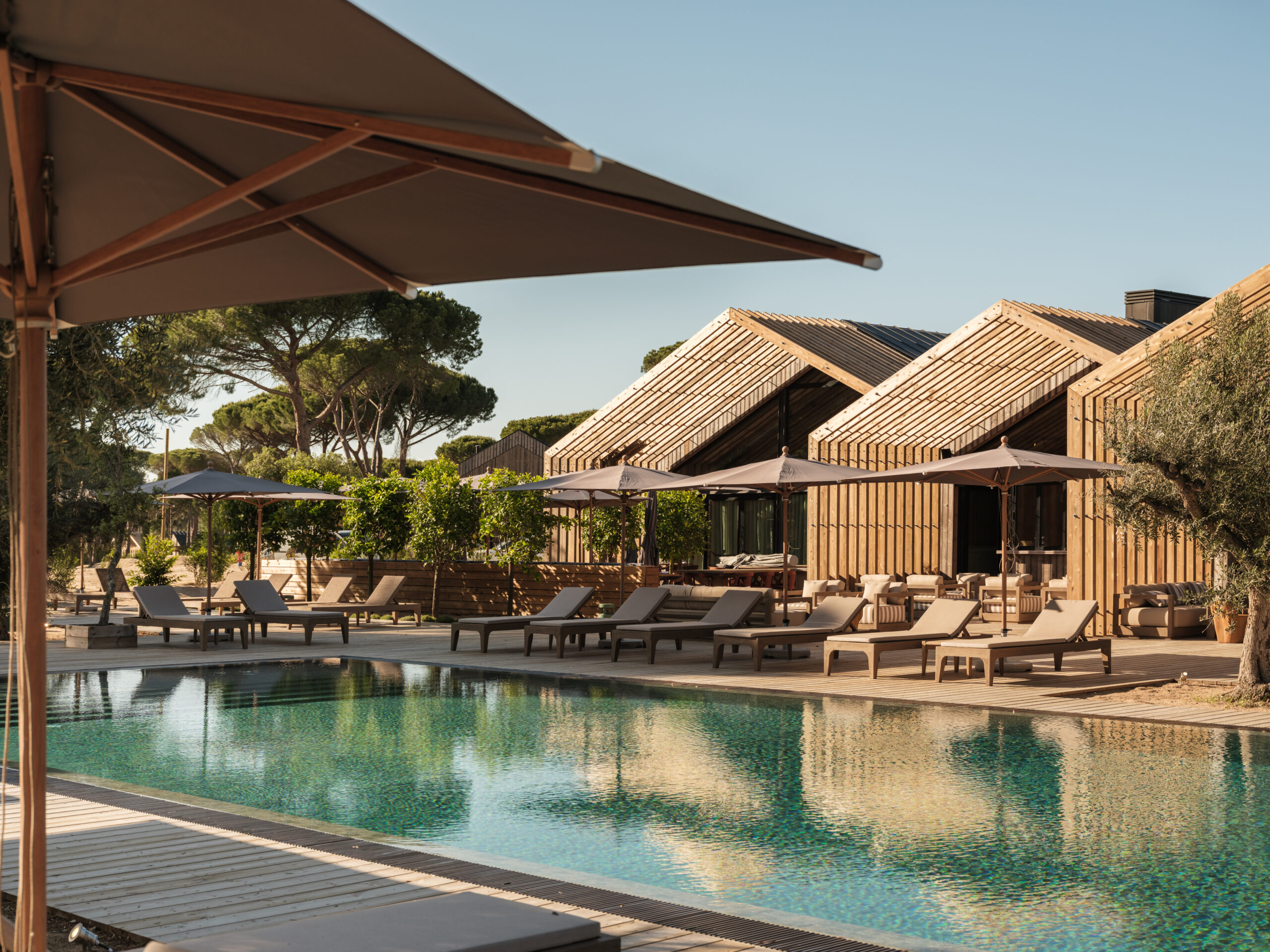 Luxury resort pool with wooden cabins and sun loungers in Comporta