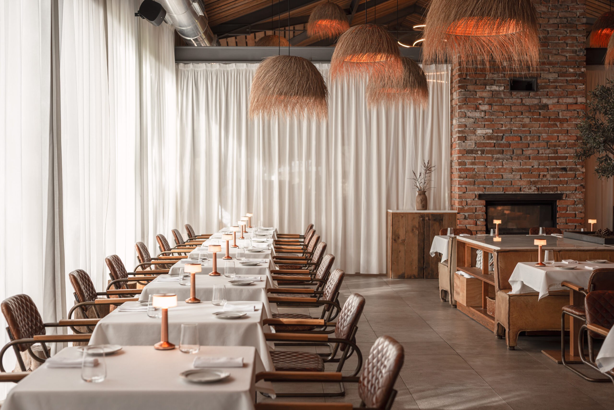 Elegant dining room with long tables, wicker lamps, and a brick fireplace