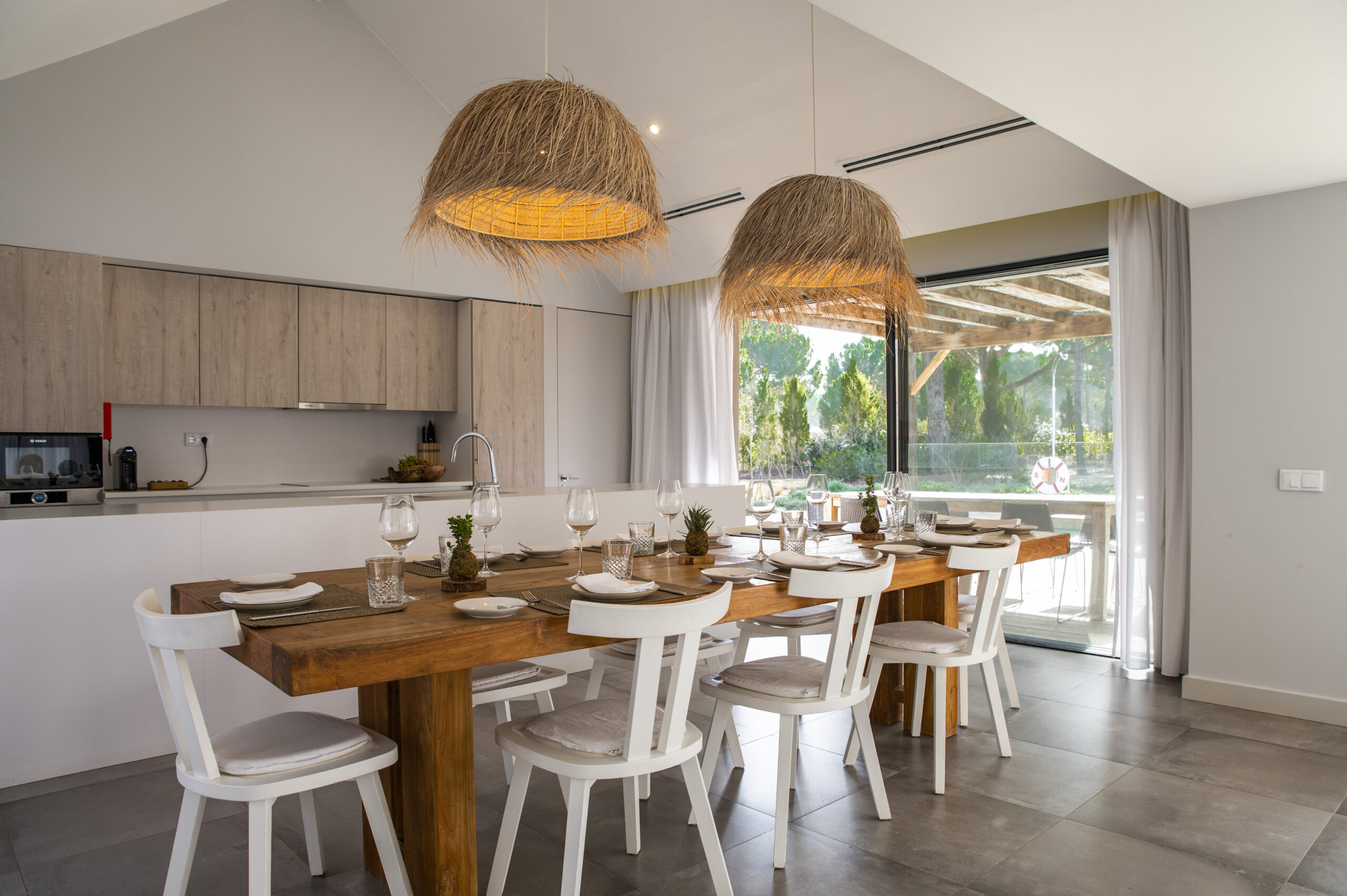 Dining room with wooden table, white chairs, and large straw pendant lights
